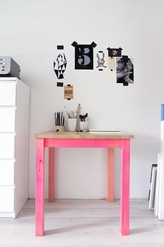 a pink table in a white room with pictures on the wall and drawers below it