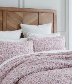 a bed with pink and white pillows on top of it next to a wooden headboard