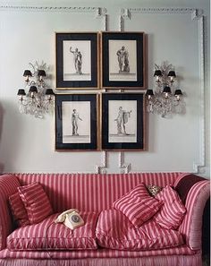 a red and white striped couch in front of pictures on the wall with chandelier