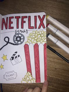 a hand holding a pencil over a book with the words netflix and popcorn on it