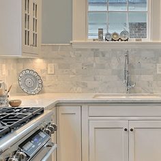 a kitchen with white cabinets and marble backsplash, stainless steel stove top oven and dishwasher