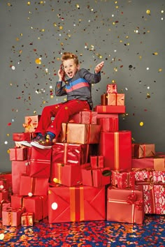 a young boy sitting on top of a pile of presents with confetti falling from the sky