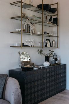 a living room filled with furniture next to a wall mounted shelf full of bottles and glasses