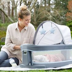 a woman sitting on the grass with a baby in a crib next to her