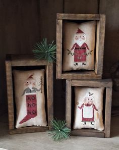 three framed cross - stitch christmas decorations with santa and snowman on them, one is holding a plant