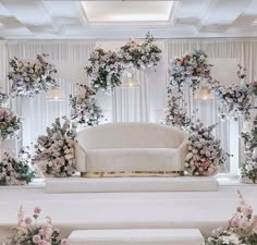 a white couch sitting in front of a flower covered stage with flowers on the wall