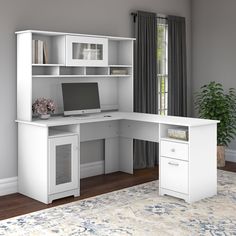 a white computer desk sitting on top of a wooden floor next to a plant and window