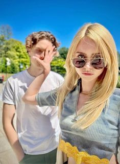 two people standing next to each other with sunglasses on and one woman holding her hand near her face