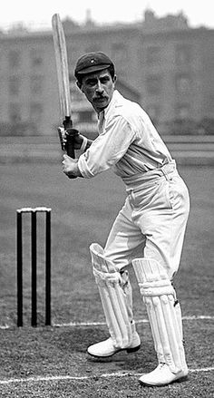 a black and white photo of a man holding a cricket bat in his hand while standing next to a ball