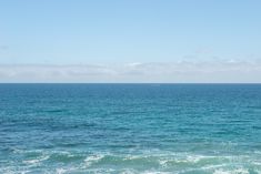 the ocean is blue and green with white clouds in the sky above it, as well as small waves on the water