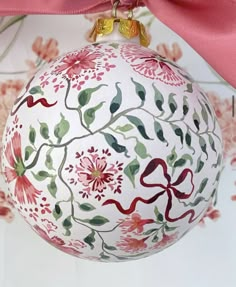 a white ornament with red and green designs on it, tied to a pink ribbon