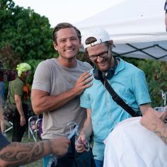 two men standing next to each other in front of a tent with people around them