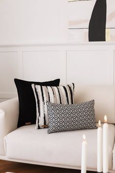 two black and white pillows sitting on top of a couch next to some lit candles