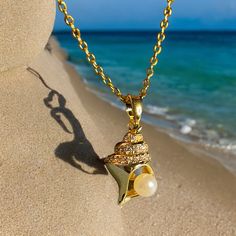 a gold necklace with a star and pearl hanging from it's side on the beach