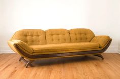 a yellow couch sitting on top of a hard wood floor next to a white wall