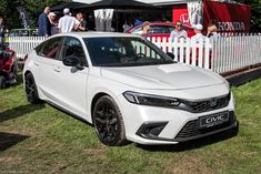 a white car parked in front of a fence with people looking at it and onlookers