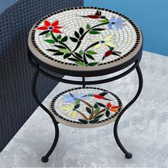 two mosaic tables with flowers on them sitting in front of a blue wall and black iron frame