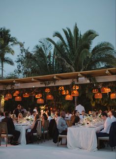 a group of people sitting around a table at a wedding reception in front of palm trees