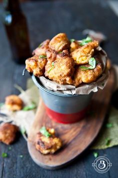 some fried food is sitting in a cup on a wooden board next to a bottle