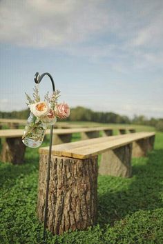 a wooden bench sitting in the middle of a field next to a tree stump with flowers hanging from it