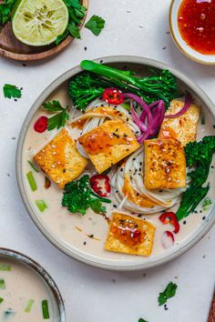 a plate with tofu, onions and broccoli on it next to dipping sauces