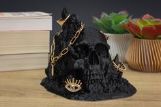 a black skull with gold chains and an evil eye on it's head sits next to a plant