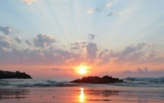 the sun is setting over an ocean with rocks in the foreground and clouds in the background