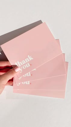 a woman's hand holding four pink thank you cards