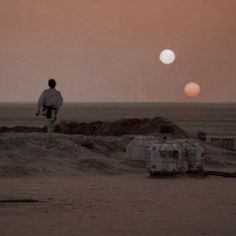 two people walking in the desert at sunset with one person looking at the sun behind them