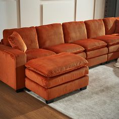 an orange sectional couch sitting on top of a wooden floor next to a white rug