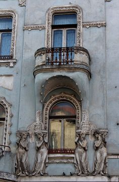 an old building with statues on the balcony and windows above it, in front of a street sign