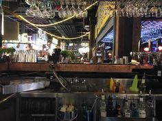 a bar with lots of wine glasses hanging from the ceiling and bottles on the counter