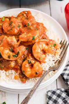 a white plate topped with shrimp and rice next to a fork on a checkered napkin