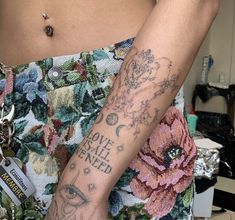 a woman's arm with tattoos on it and a flowered skirt in the background