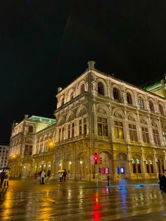 people are walking around in the rain near an old building with lights on at night