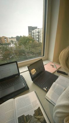 a woman sitting at a table with two laptops and books in front of her