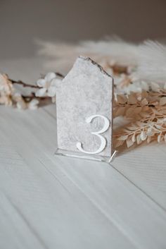 a white house shaped table number sitting next to dried flowers