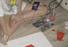 a woman sitting on the floor with her legs crossed, painting and holding a paintbrush