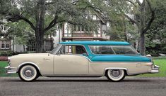 an old blue and white station wagon parked in front of a large house with trees