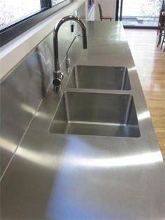 a stainless steel kitchen sink with two faucets in front of the counter top