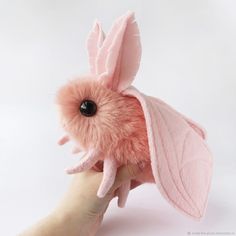 a hand holding a pink stuffed animal with leaves on it's head and ears