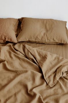 an unmade bed with brown sheets and pillows