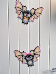 two small bats hanging on the side of a white door with pink flowers in their hair