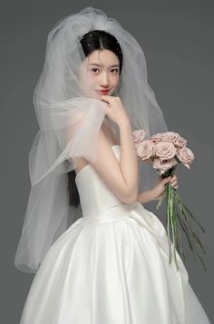 a woman in a white wedding dress holding a bouquet of flowers and wearing a veil