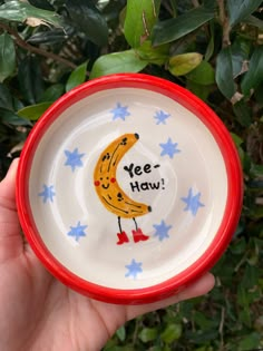 a hand holding a small bowl with an image of a yellow banana on it that says yee - haw