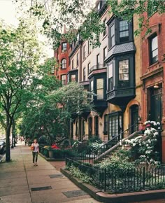 a woman walking down a sidewalk next to tall brick buildings with balconies and windows