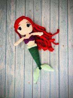 a crocheted mermaid doll laying on top of a wooden floor next to a wall