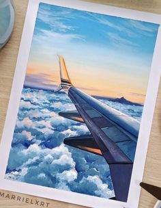 an airplane wing is shown above the clouds and watercolors on paper, next to a pair of scissors