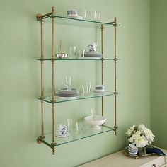 the shelves are filled with glassware and vases on top of each shelf in front of a green wall