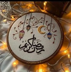 an embroidered hoop with arabic writing on it and lights in the back ground behind it